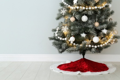 Photo of Decorated Christmas tree with red skirt indoors, space for text