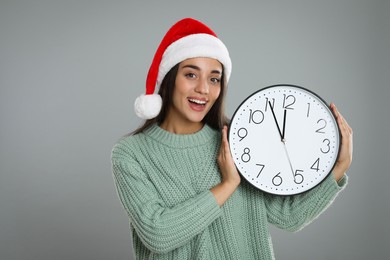 Photo of Woman in Santa hat with clock on grey background. New Year countdown