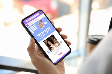 Image of Young man visiting online dating site via smartphone indoors, closeup