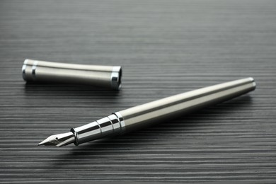 Photo of Stylish silver fountain pen on black wooden table, closeup