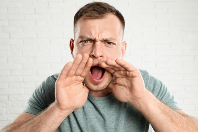 Photo of Emotional young man screaming near white brick wall