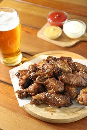 Photo of Tasty roasted chicken wings served with beer on wooden table