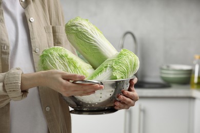 Photo of Woman holding fresh chinese cabbages in kitchen, closeup. Space for text