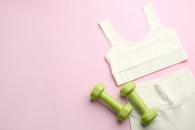 Photo of Sportswear and dumbbells on pink background, flat lay with space for text. Gym workout