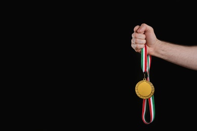 Photo of Man holding golden medal on black background, closeup. Space for design