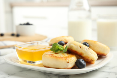 Photo of Delicious cottage cheese pancakes with blueberries, mint and honey on white marble table