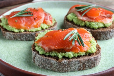 Photo of Delicious sandwiches with salmon, avocado and rosemary on plate, closeup
