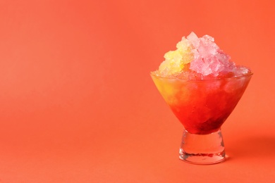 Photo of Rainbow shaving ice in glass dessert bowl on orange background, closeup. Space for text