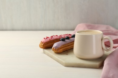 Photo of Cup of coffee and delicious eclairs covered with glaze on white wooden table. Space for text