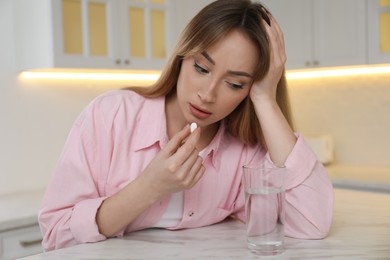 Photo of Young woman taking abortion pill in kitchen