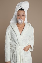 Photo of Young woman in bathrobe blowing chewing gum on brown background