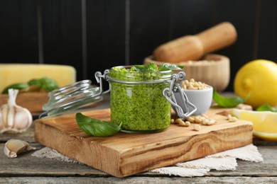 Photo of Delicious pesto sauce in jar and ingredients on wooden table