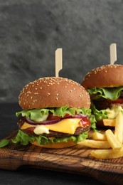 Photo of Delicious burgers with beef patty and french fries on dark table