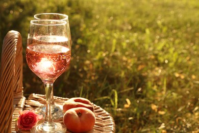 Photo of Glassesdelicious rose wine, flower and peaches on wicker basket outside. Space for text