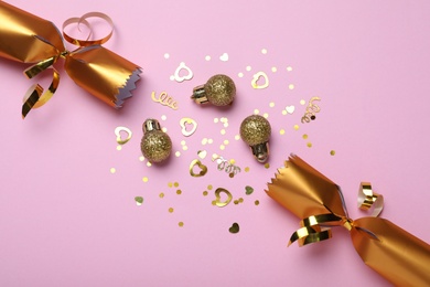 Photo of Open golden Christmas cracker and decorations with shiny confetti on pink background, flat lay