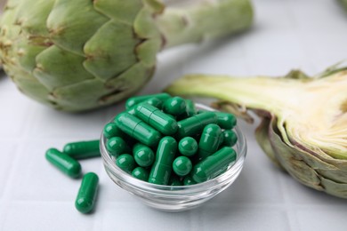 Photo of Bowl with pills and fresh artichokes on white tiled table, closeup