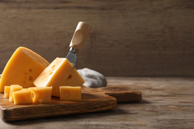 Photo of Serving board with delicious cheese on wooden table, space for text