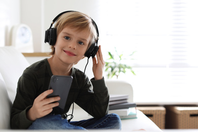 Photo of Cute little boy with headphones and smartphone listening to audiobook at home