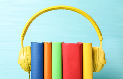 Photo of Books and modern headphones on light blue wooden background, closeup