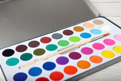 Photo of Watercolor palette with brush on white wooden table, closeup