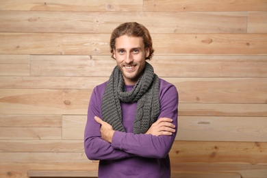 Photo of Handsome young man in warm sweater with scarf on wooden background