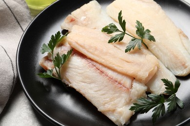 Photo of Plate with raw cod fish and parsley on light table, closeup