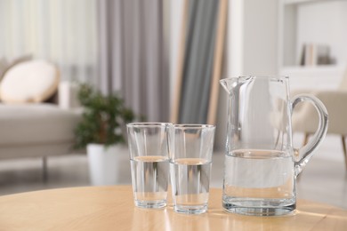 Photo of Jug and glasses with clear water on table indoors, closeup. Space for text