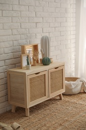 Photo of Stylish room interior with wooden cabinet near white brick wall