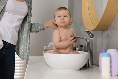 Photo of Mother washing her little baby in sink at home