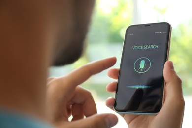 Photo of Young man using voice search on smartphone indoors, closeup