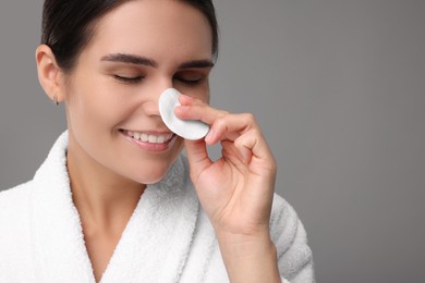 Photo of Young woman cleaning her face with cotton pad on grey background. Space for text