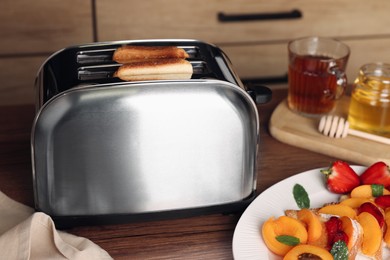 Photo of Roasted bread in toaster, tea and sandwiches on wooden table. Tasty breakfast