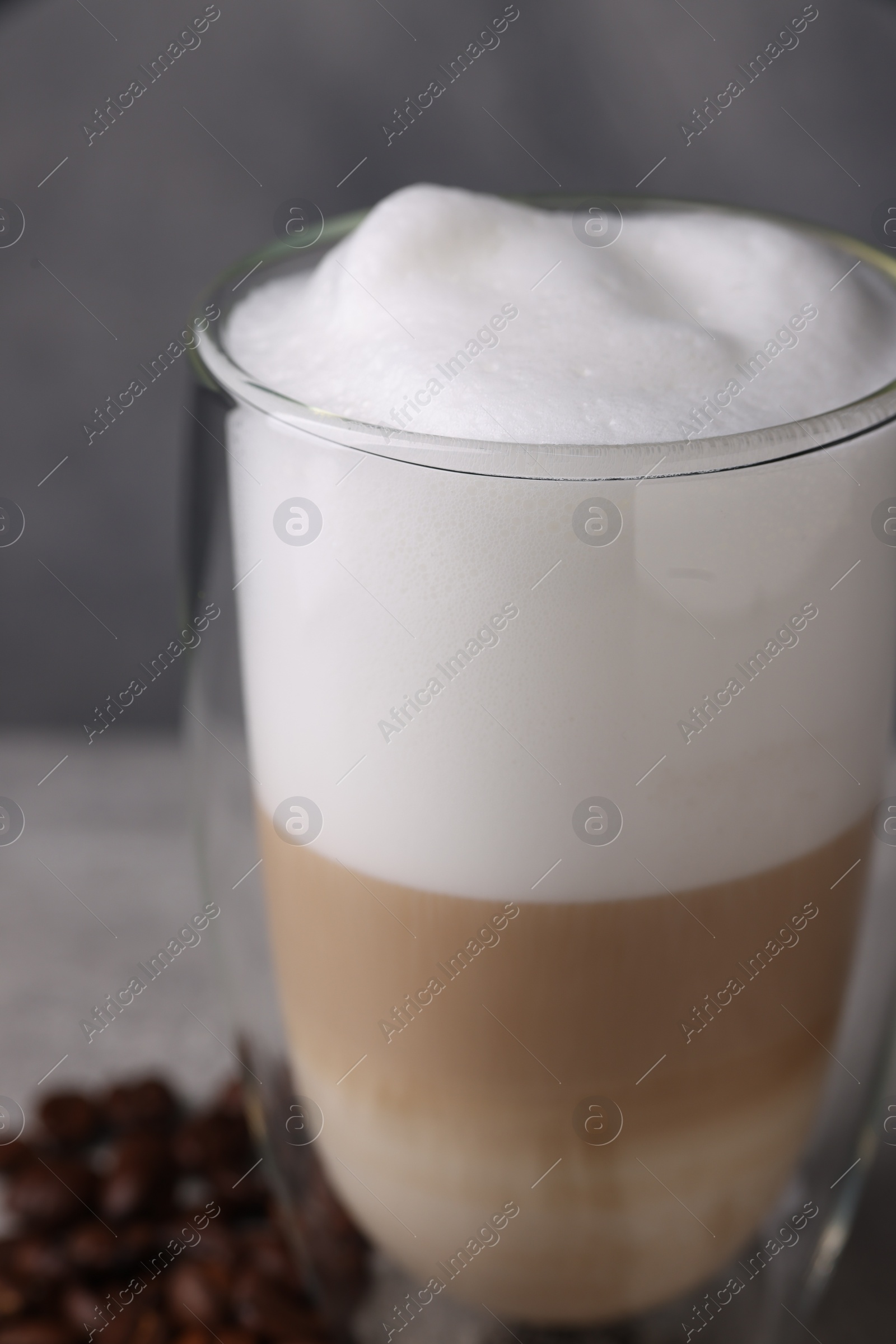 Photo of Aromatic latte macchiato in glass and coffee beans on light grey table, closeup