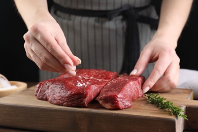 Photo of Woman salting fresh raw beef steak at table, closeup