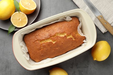 Photo of Tasty lemon cake in baking dish and citrus fruits on grey table, flat lay