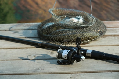 Photo of Fishing rod and fresh fish on wooden pier near pond