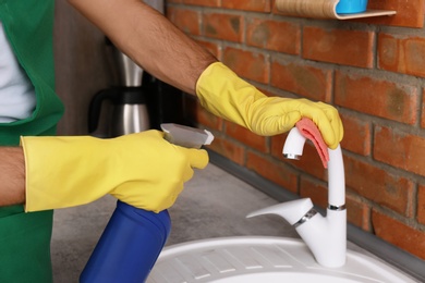 Photo of Man cleaning tap with rag in kitchen, closeup