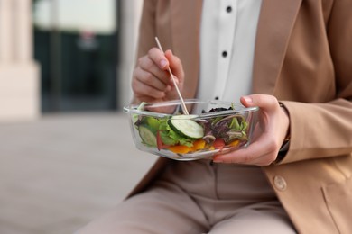 Businesswoman with container of salad having lunch outdoors, closeup