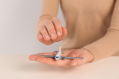 Photo of Woman covering toy plane on light background, closeup view with space for text. Travel insurance concept