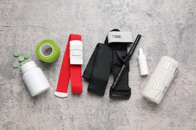 Photo of Tourniquet, elastic bandage, adhesive plaster and pills on light grey table, flat lay