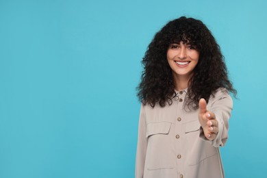 Photo of Happy young woman welcoming and offering handshake on light blue background, space for text