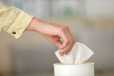 Photo of Woman taking paper tissue from holder indoors, closeup