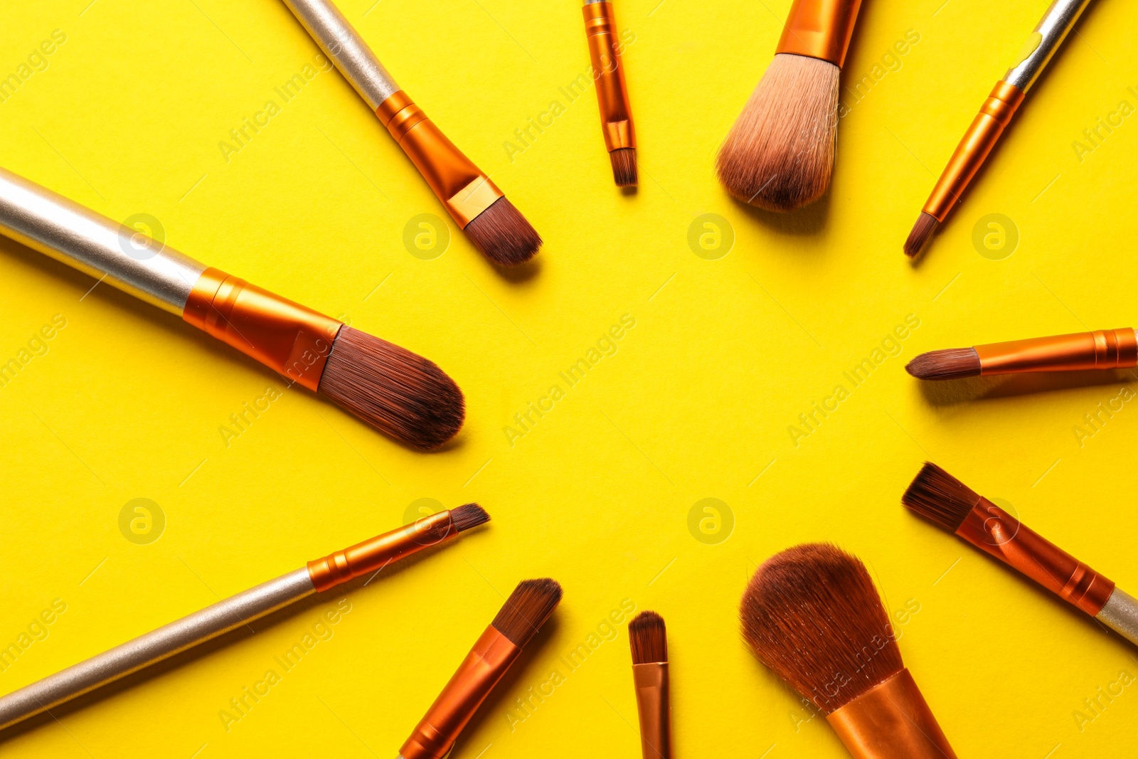 Photo of Different makeup brushes on yellow background, flat lay. Space for text