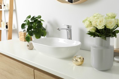 Photo of Vase with beautiful white roses and toiletries near sink in bathroom