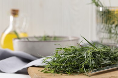 Photo of Fresh tarragon sprigs and knife on white wooden table, closeup