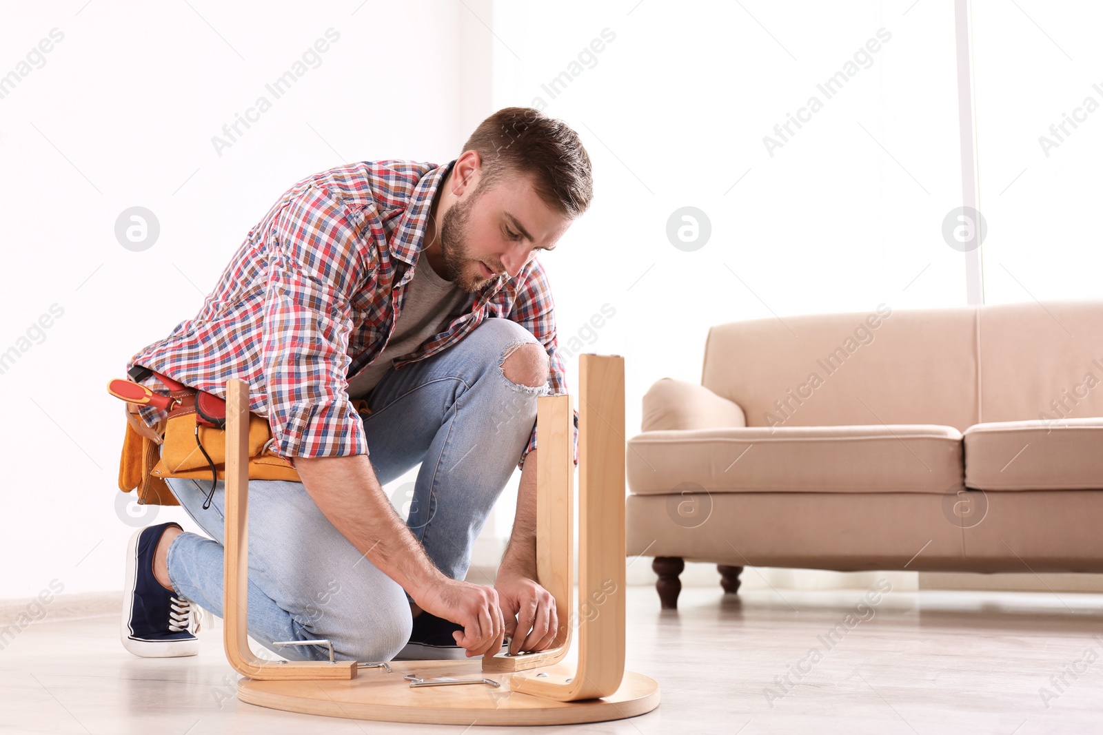 Photo of Young man working with wooden chair indoors. Space for text