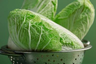 Photo of Fresh Chinese cabbages in colander on green background, closeup