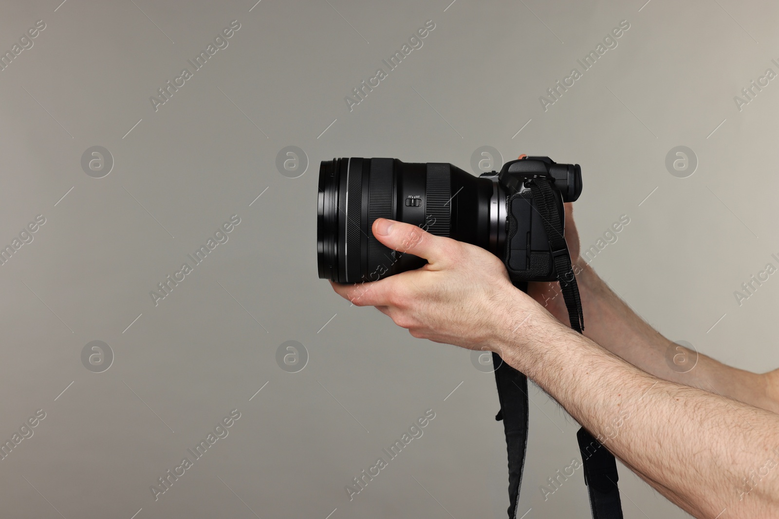 Photo of Photographer holding camera on grey background, closeup. Space for text