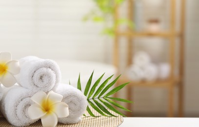 Photo of Spa composition. Towels, plumeria flowers and palm leaves on white table in bathroom, space for text