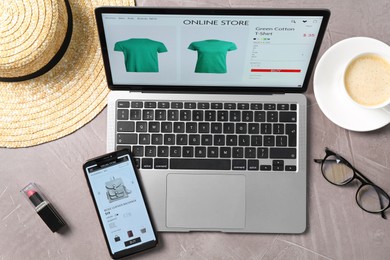 Photo of Online store website on laptop screen. Computer, smartphone, coffee and accessories on grey table, flat lay